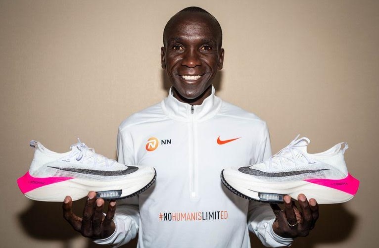 Eliud Kipchoge segurando dois pés do tenis alphaflt da nike com detalhes rosa