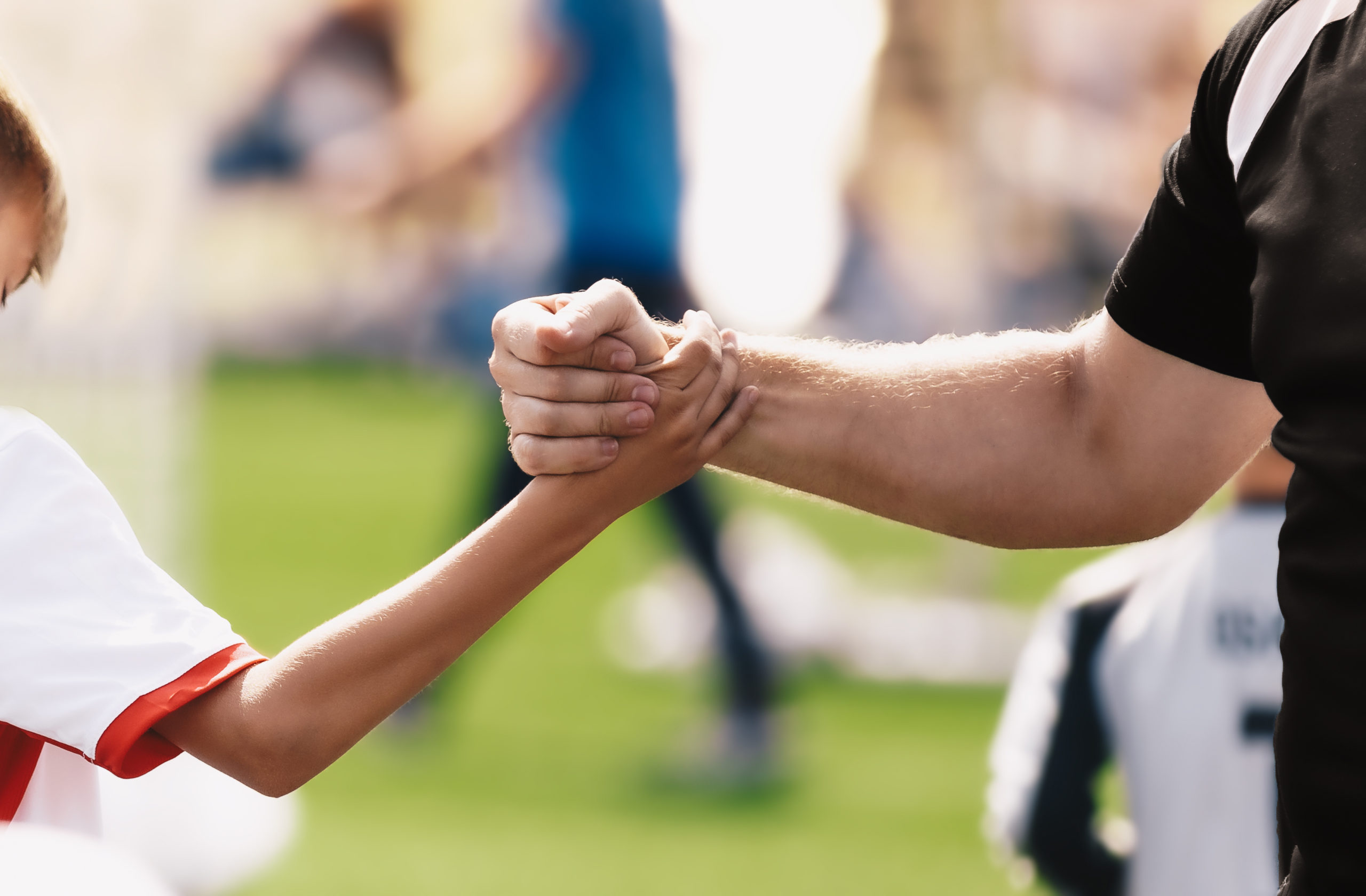 Dois braços fazendo um aperto de mão dentro de um campo de futebol