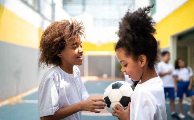 Duas meninas na aula de educação física com uma bola de futebol na mão