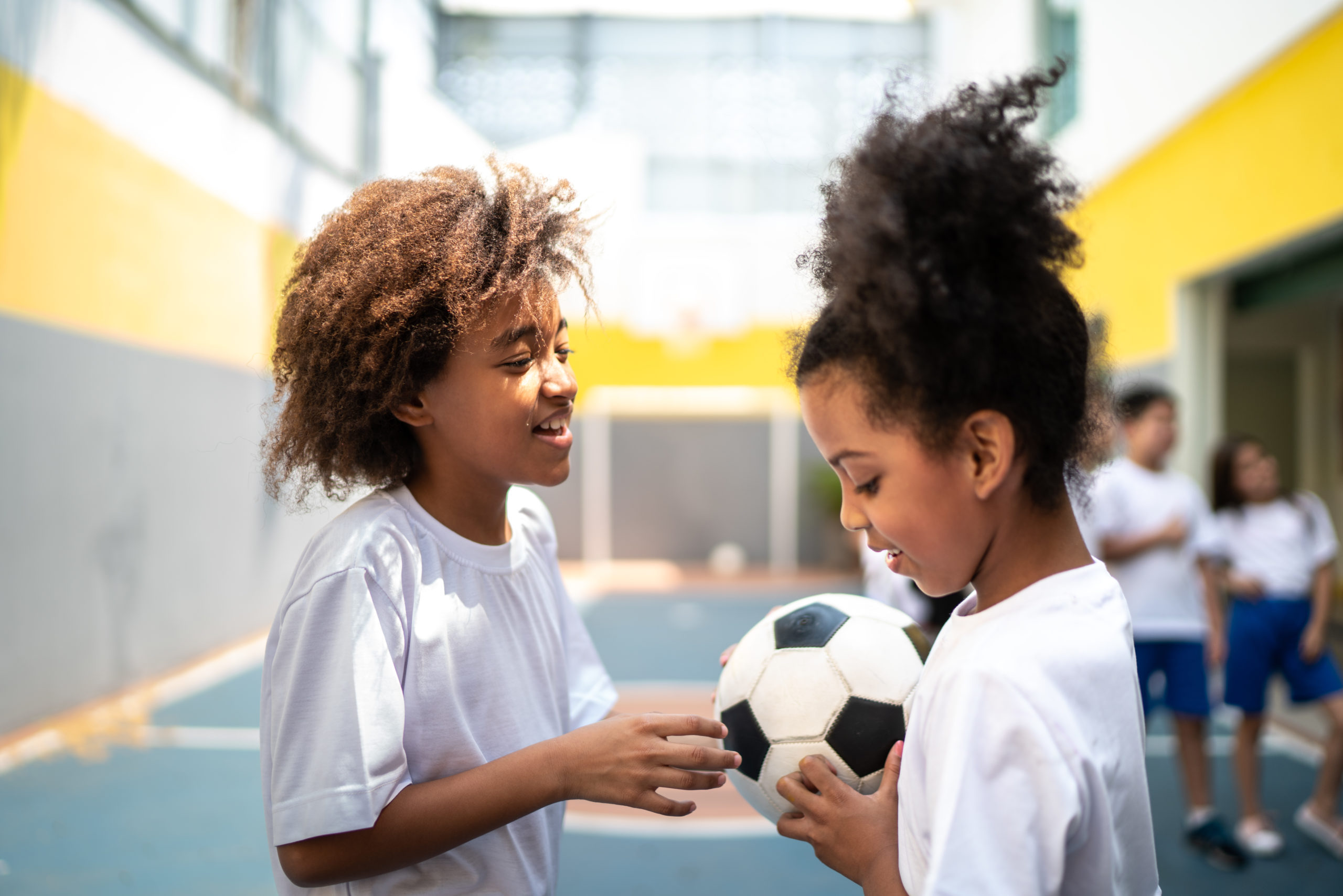 Duas meninas na aula de educação física com uma bola de futebol na mão