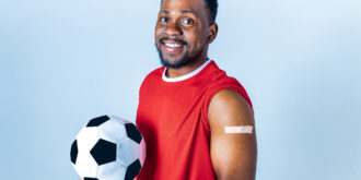 vacina esporte atividade física homem com bola de futebol na mão e braço com bandaid após vacina