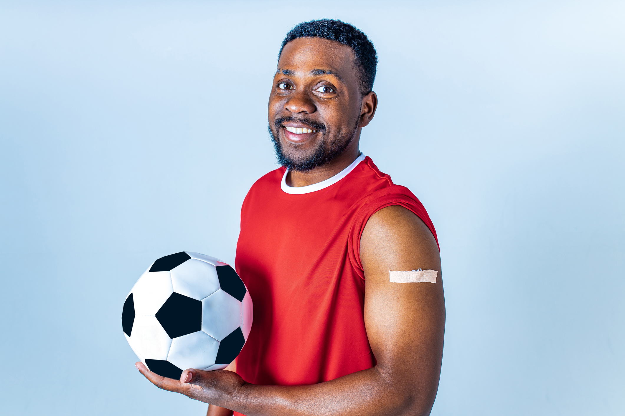 vacina esporte atividade física homem com bola de futebol na mão e braço com bandaid após vacina