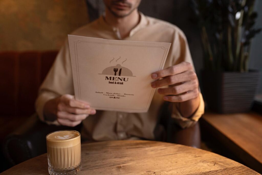 Homem segurando um cardápio/menu de papel branco sentado em uma mesa de restaurante